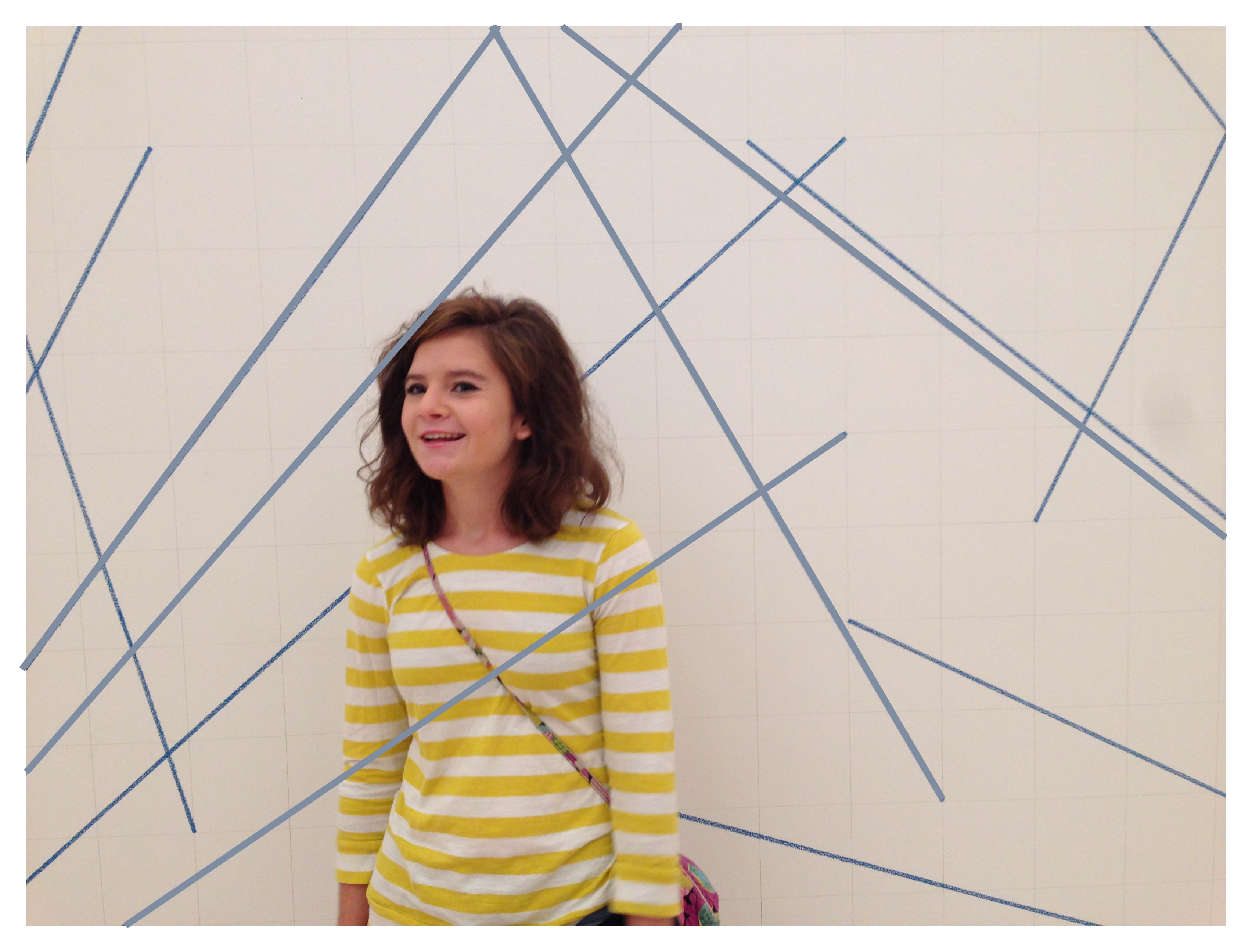 Brooke is standing in front of Sole LeWitt's Wall Drawing 273. This drawing is of blue lines on a white wall, but some of the lines have been edited to go over Brooke. She is wearing a yellow and white striped shirt.
