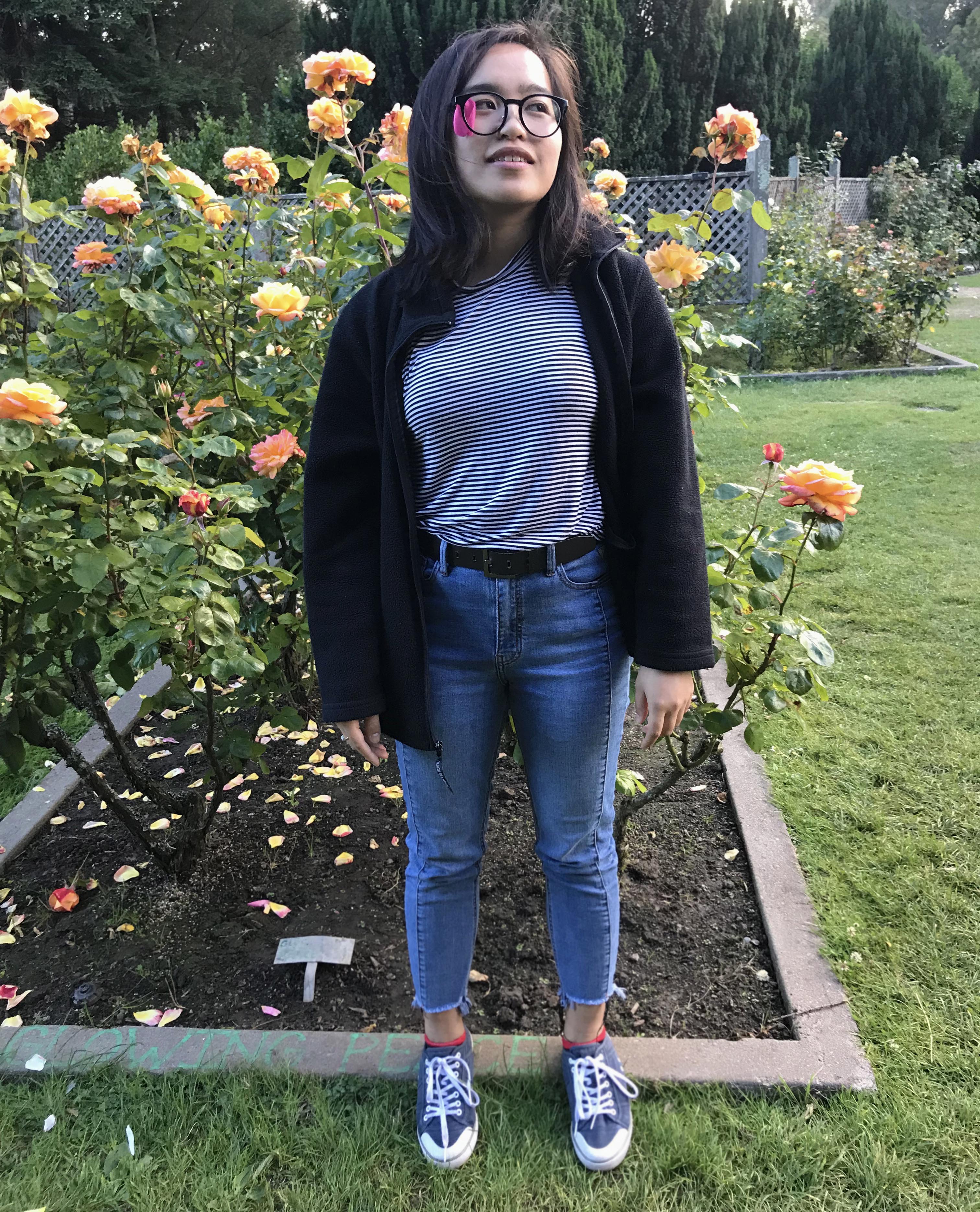 Awkward girl standing in front of roses. A rose petal is stuck in her glasses.