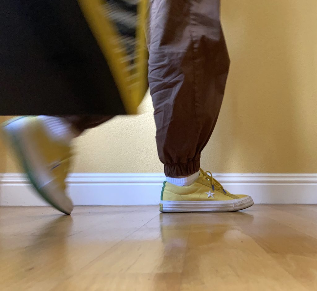 A pair of feet walking by carrying a bag. Yellow and brown colors are complemented by white.