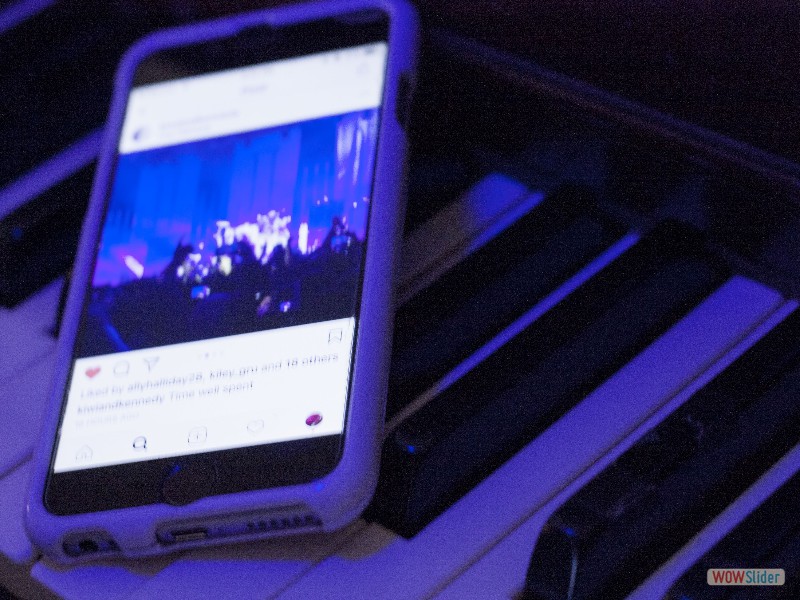 Phone open to an Instagram post about a concert on top of a piano keyboard