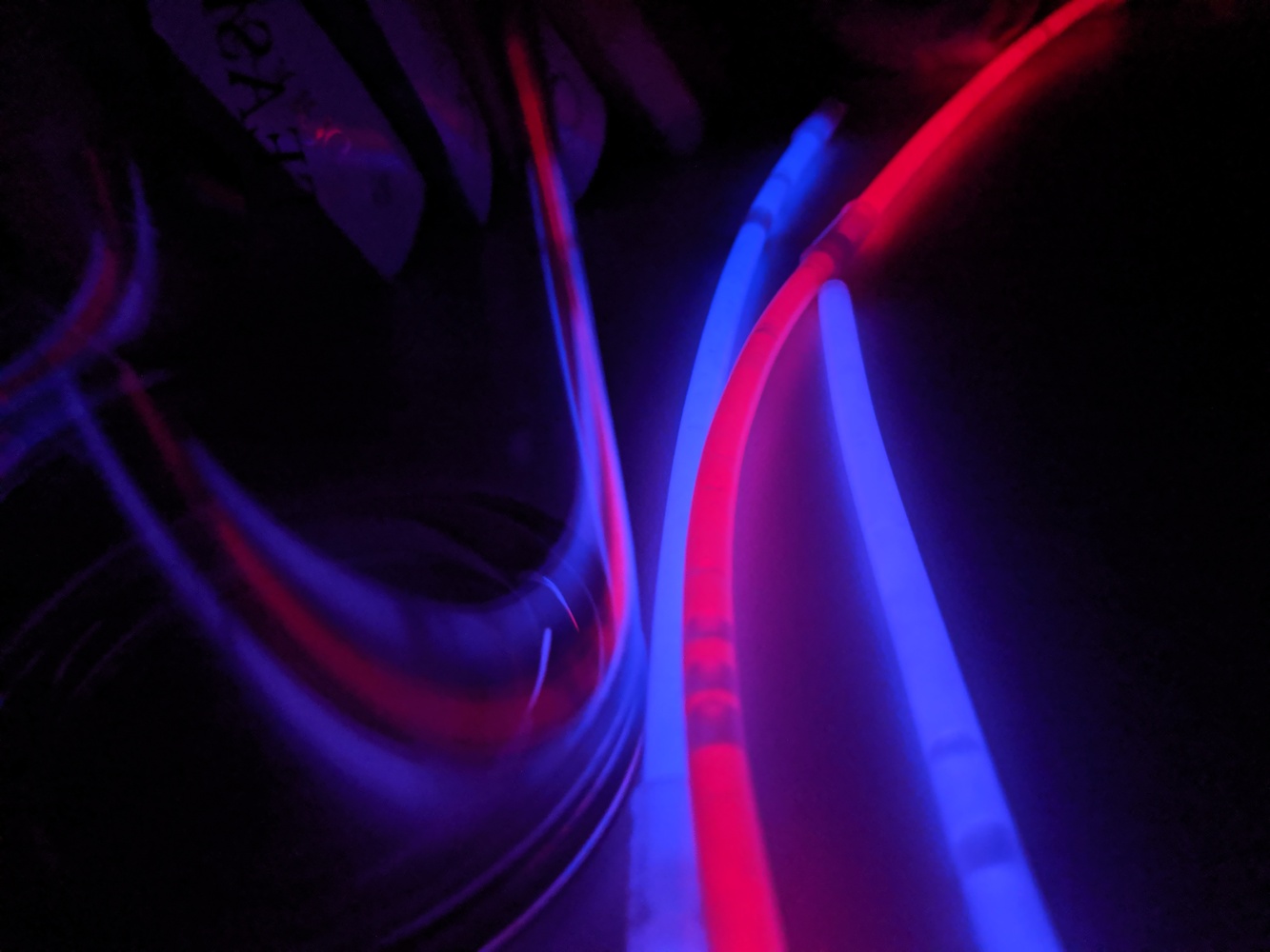 An almost abstract image of glowing glowsticks reflecting on a clear surface in the dark,creating multiple leading lines.