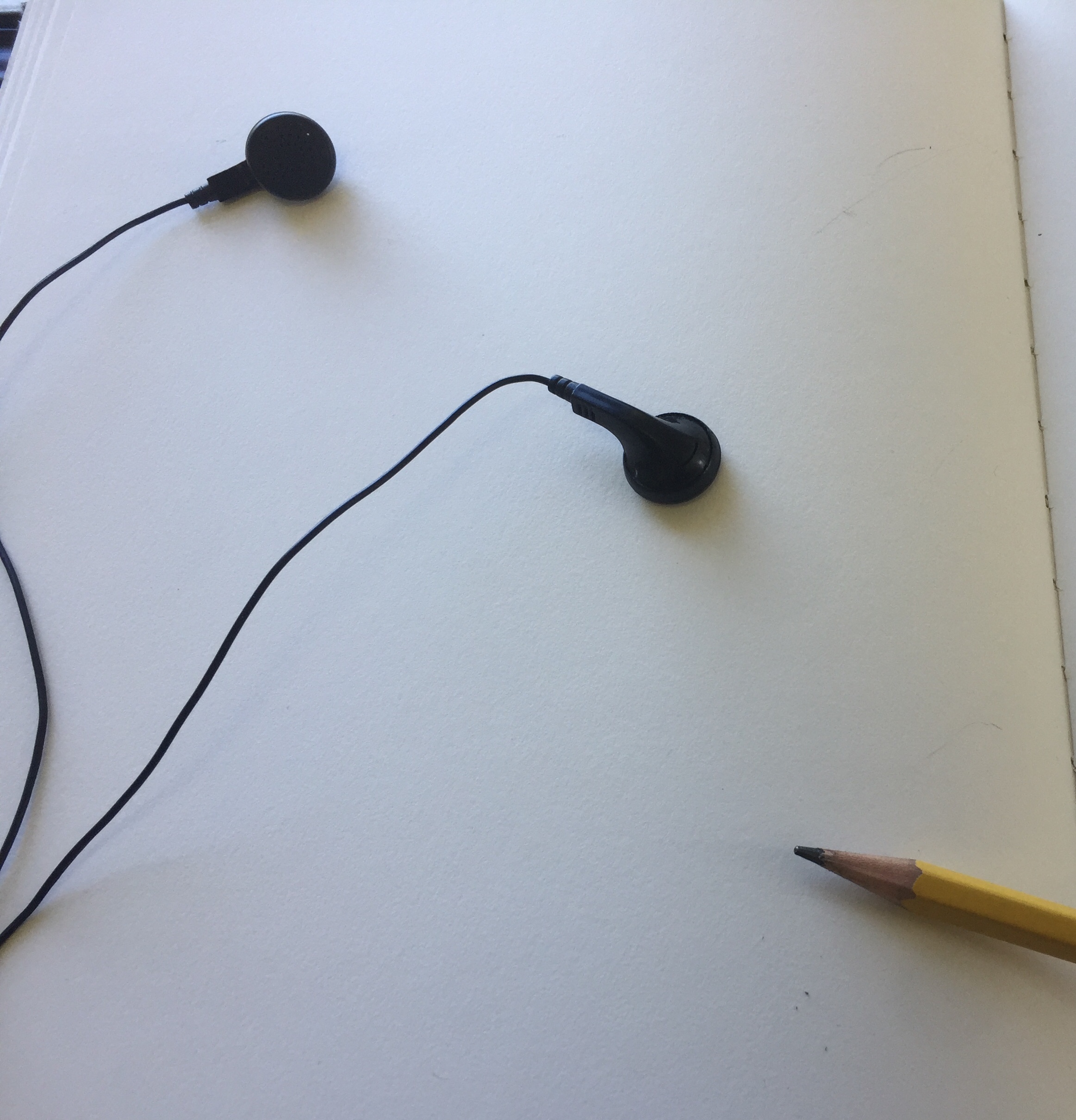 A picture of a page of a blank sketchbook, with earbuds and a pencil placed in the photograph.