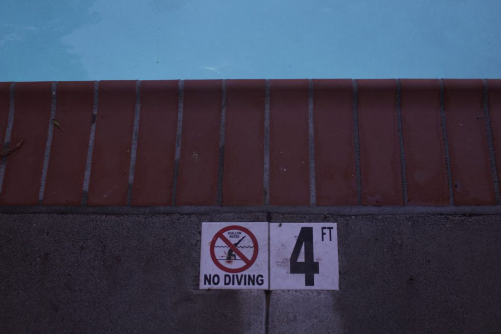A photo Self Portrait. The photo shows the edge of a pool with a No Diving sign.