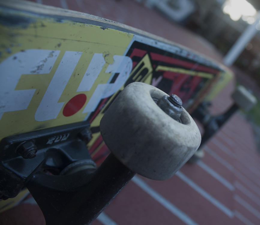 This a close up photo of a skateboard on it's side with focus on one of the front wheels. 