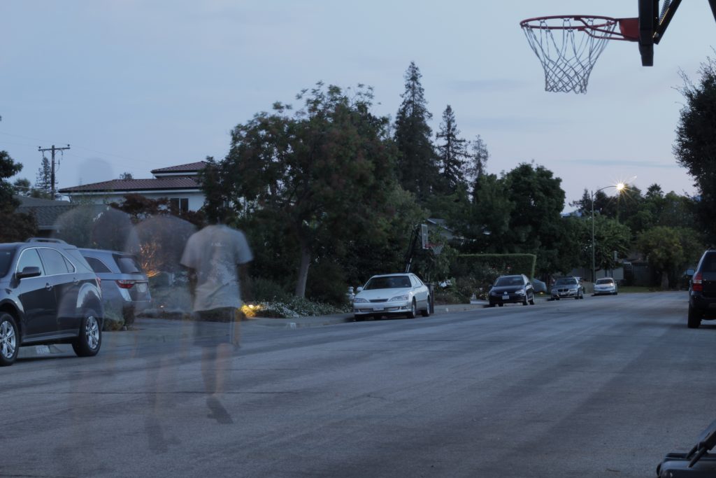 Shows a ghosting image of a boy, walking into the street at night. The street has no cars in it.