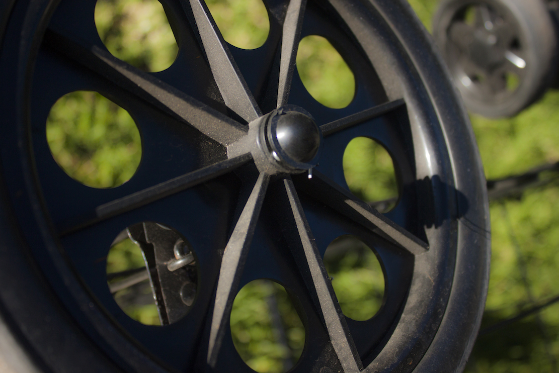 This is a photo of a black cart wheel on a grassy background in the sun.
