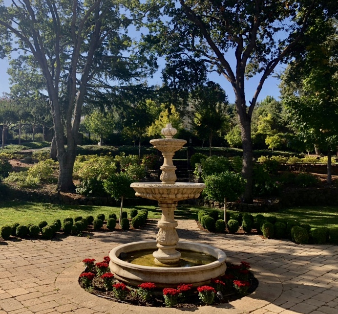This image shows a fountain centered by symmetric trees and bushes on either side creating a continuous circular effect.