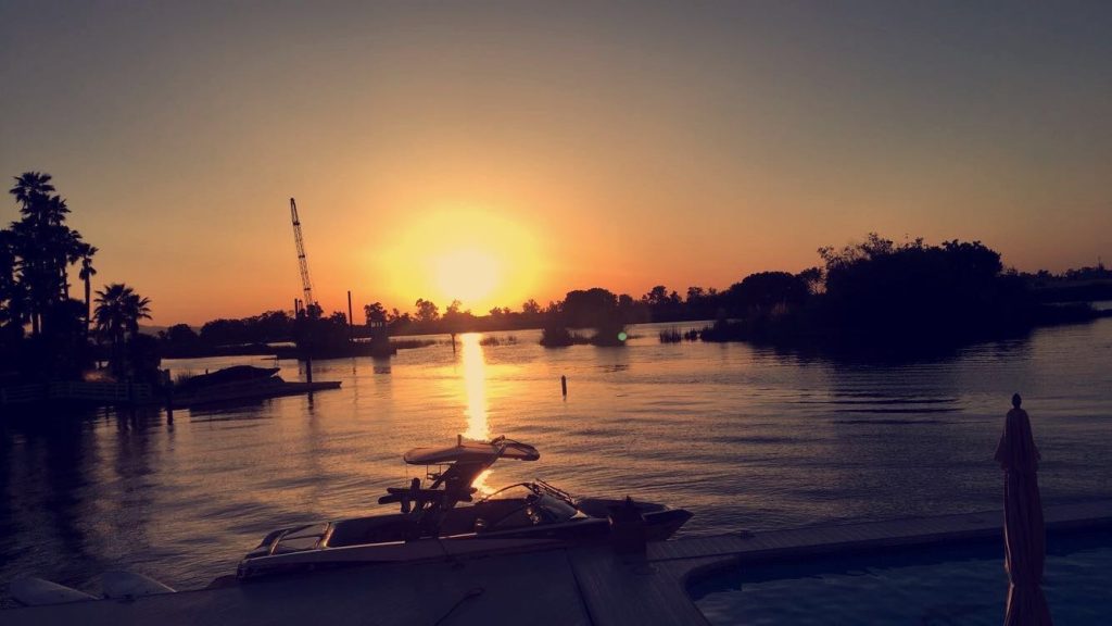 This image shows a beautiful orange sunset with a boat in the foreground. There is some sort of lake or delta that the boat is in.