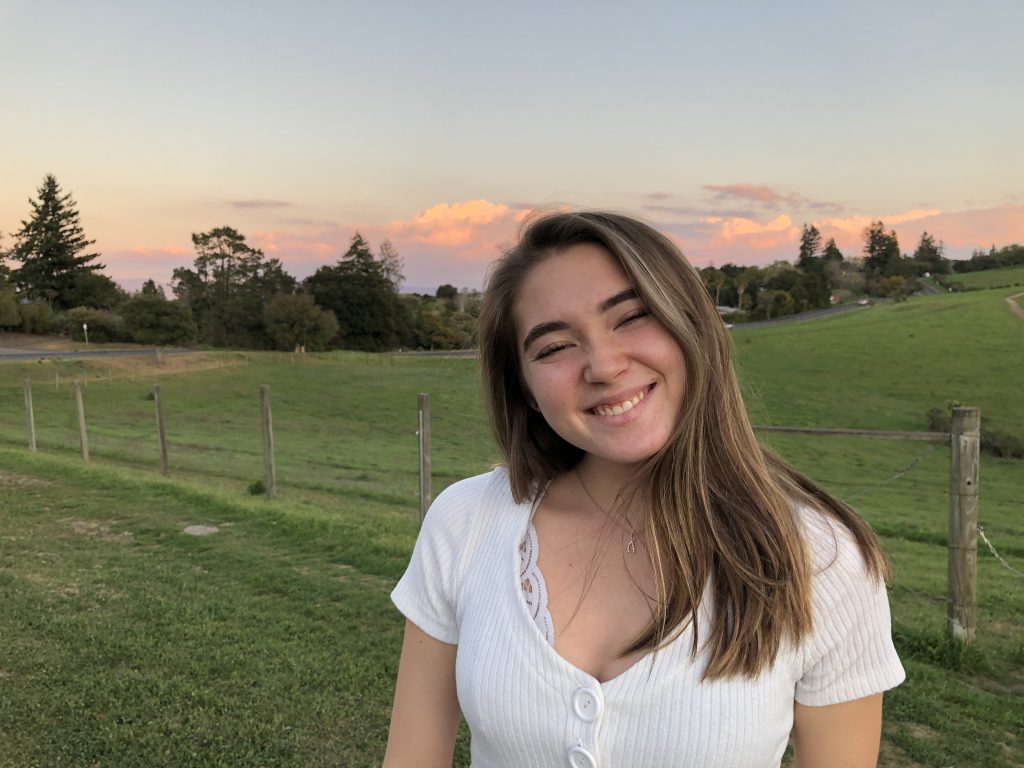 a girl smiling big and carefree on a field with a sunset in the background