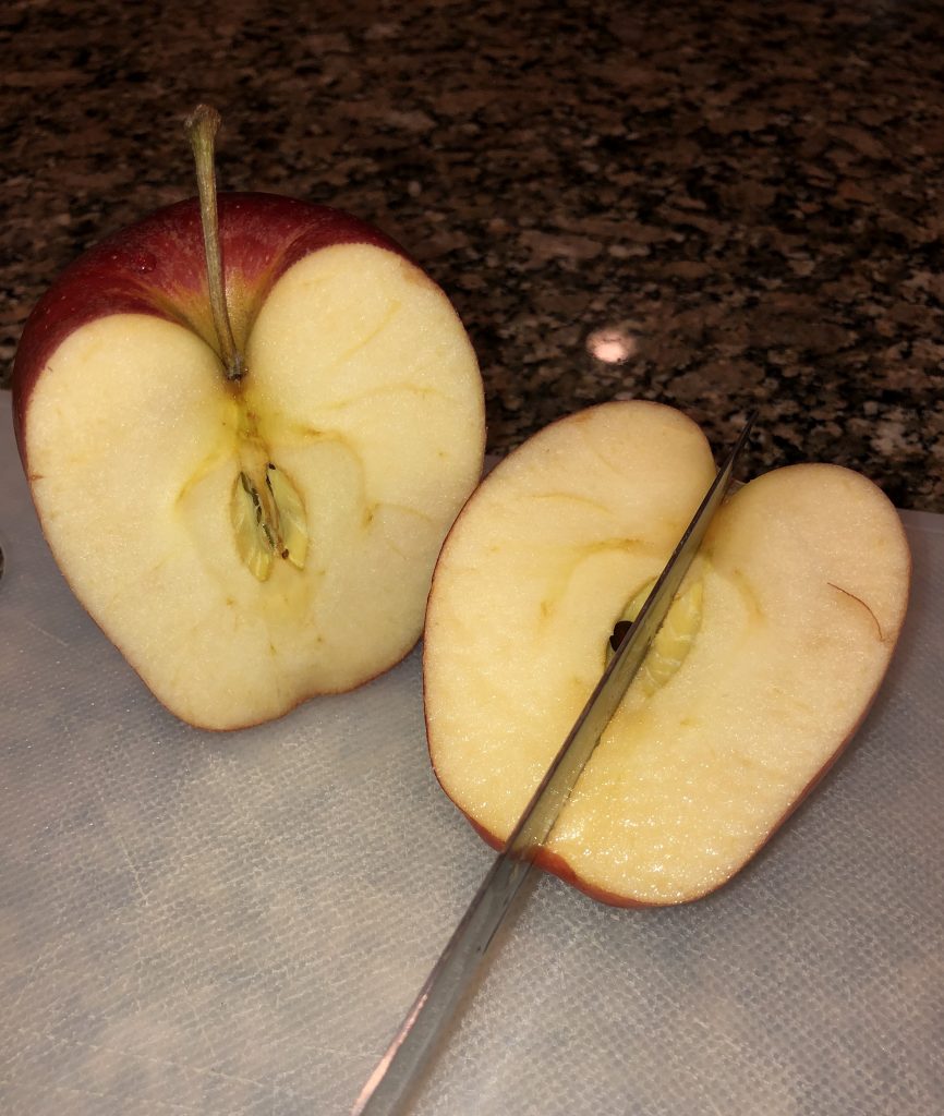 image of two halves of an apple placed next to each other with a knife about to cut one of the halves into fourths acting as a leading line