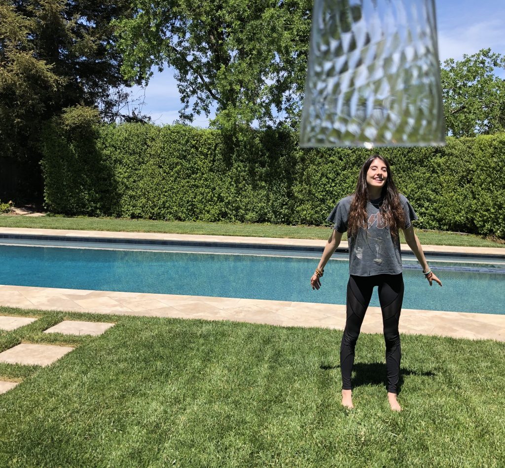 This image depicts my sister standing on the grass with a plastic cup up in the top right frame looking like it is going to fall on to her