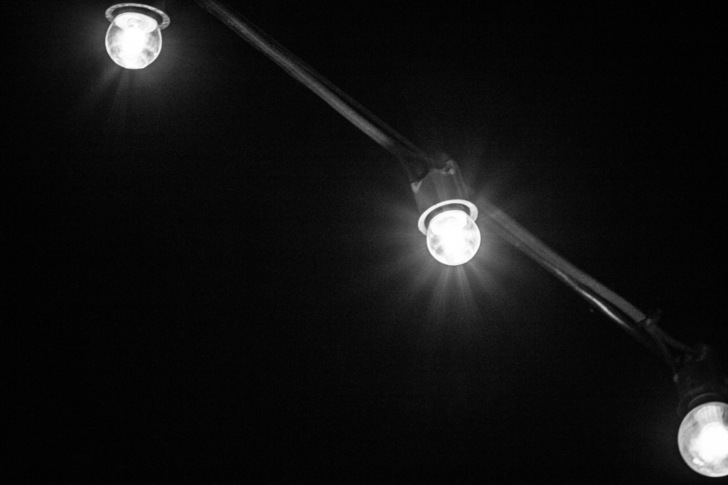 A black and white picture of a lightbulb on a string in the sky. 