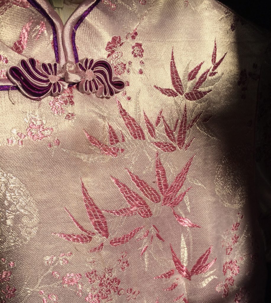 A photo of the details of a traditional Chinese silk dress, chi pao. It’s purple silk fabric in the sun with intricate details.
