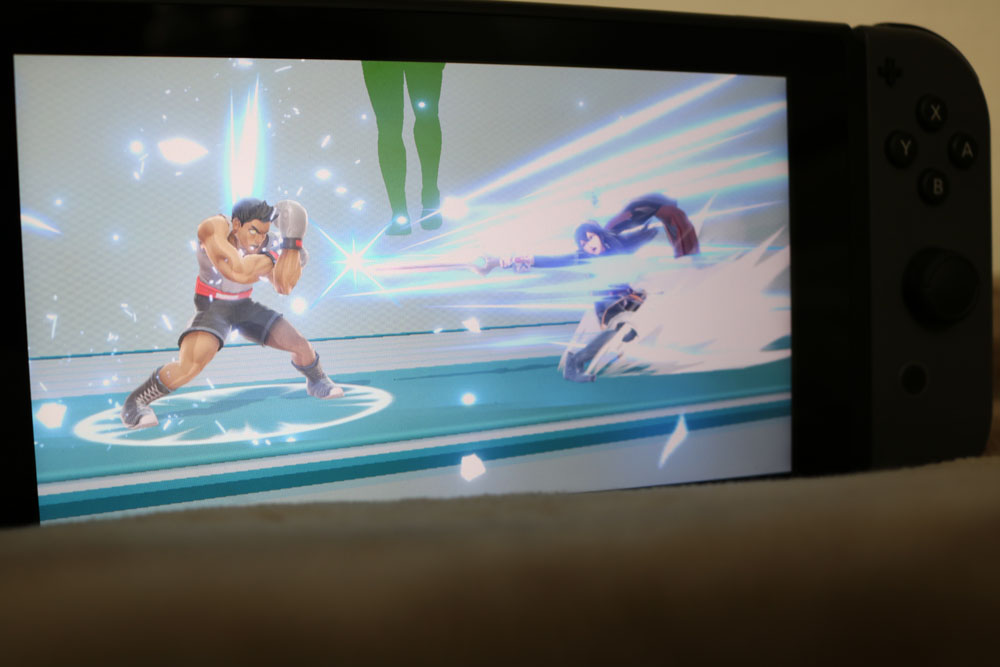 Photo of a Nintendo Switch. with an image of a battle between Little Mac and Lucina on the screen.