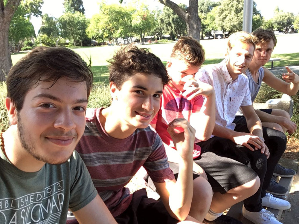 Photo of 5 friends sitting side by side on a bench in a park.