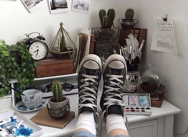 A pair of converse on a desk with some cacti and paint supplies.