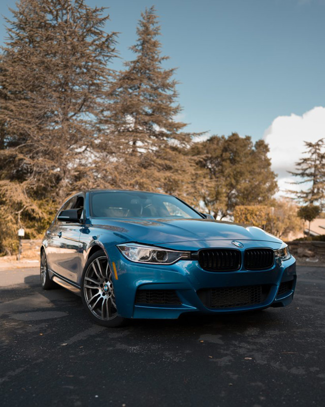 Photo of a BMW, color is blue and its facing sideways. The front wheels are faced towards the camera.