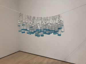 Water bottles that are all filled a small amount with a blue liquid, hung on a wire. 