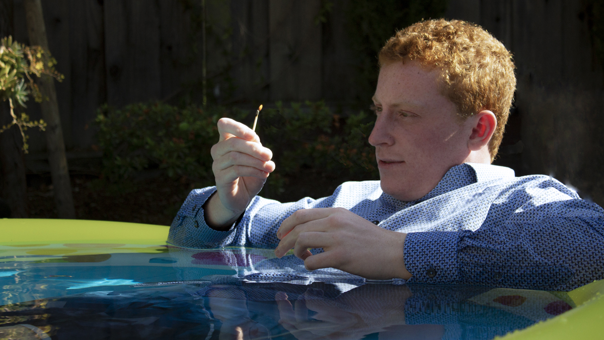 The image shows a person sitting in a kiddie pool lighting a match