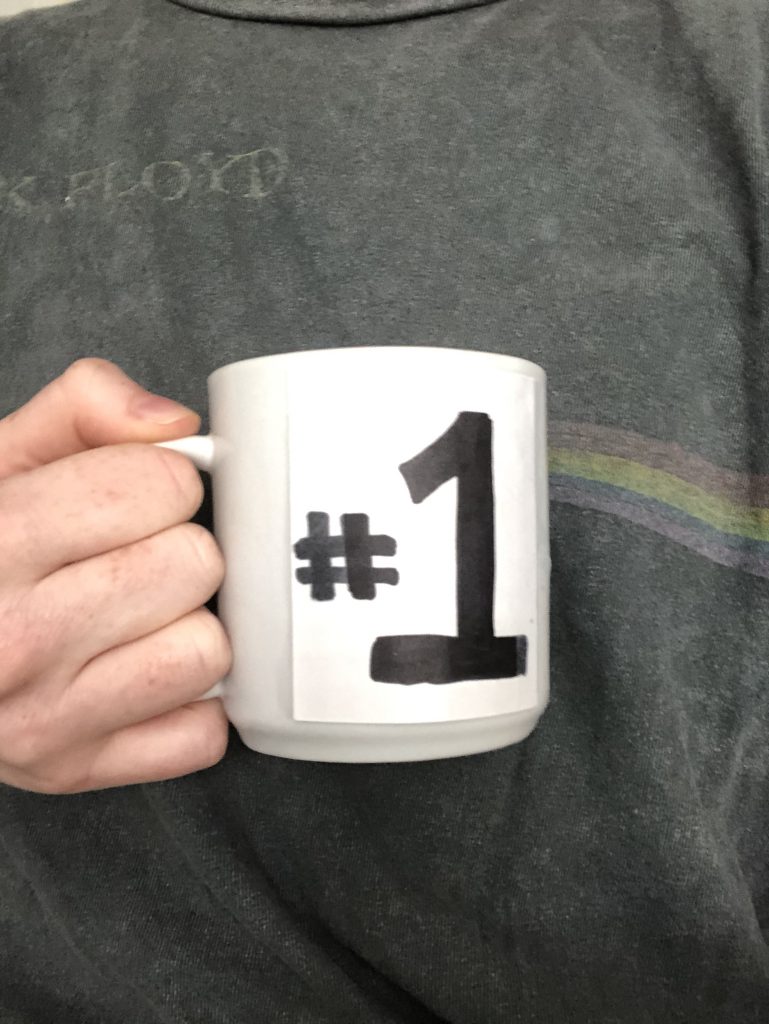 The image shows a person holding a mug with "#1" on it. 