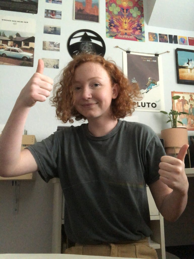 The image shows me giving a thumbs up in front of a wall covered in posters.